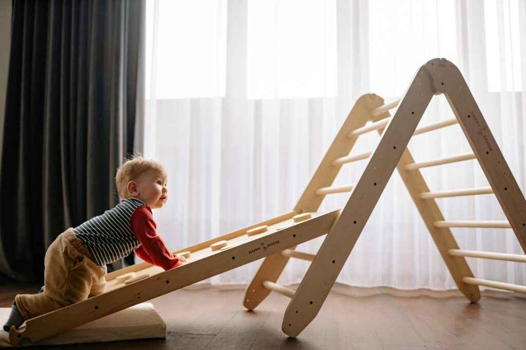 A baby joyfully climbs a wooden play structure inside a well-lit room.